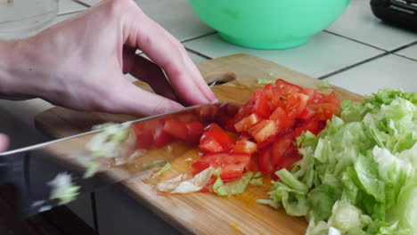 cierra las manos cortando tomates y cortando verduras con un cuchillo de cocina mientras preparas una comida vegana saludable en una tabla de cortar de madera