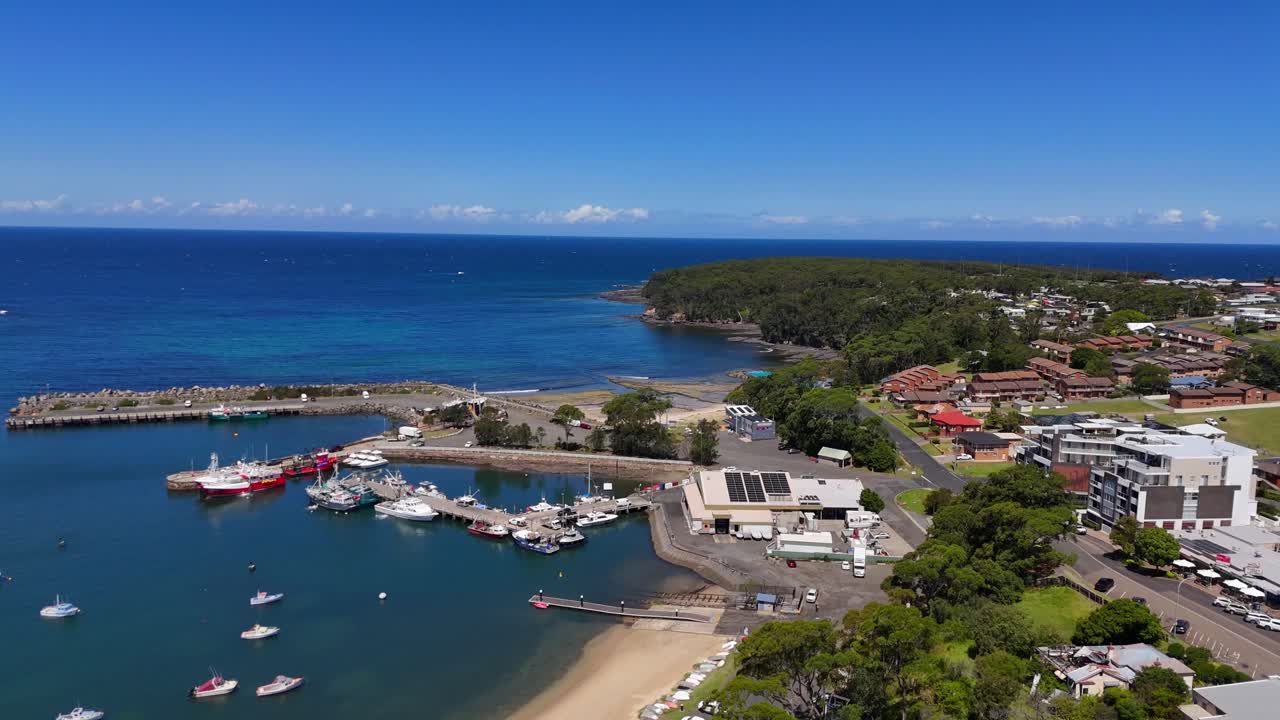 Wide aerial backside of Ulladulla coastal town with harbour and surrounding headlands, out to ocean