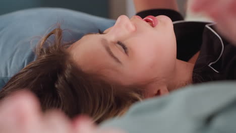 close up of young woman lying on bed while singing with expressive eyes and gentle smile, another person lying beside her, indoor scene captures calm, musical bonding in soft