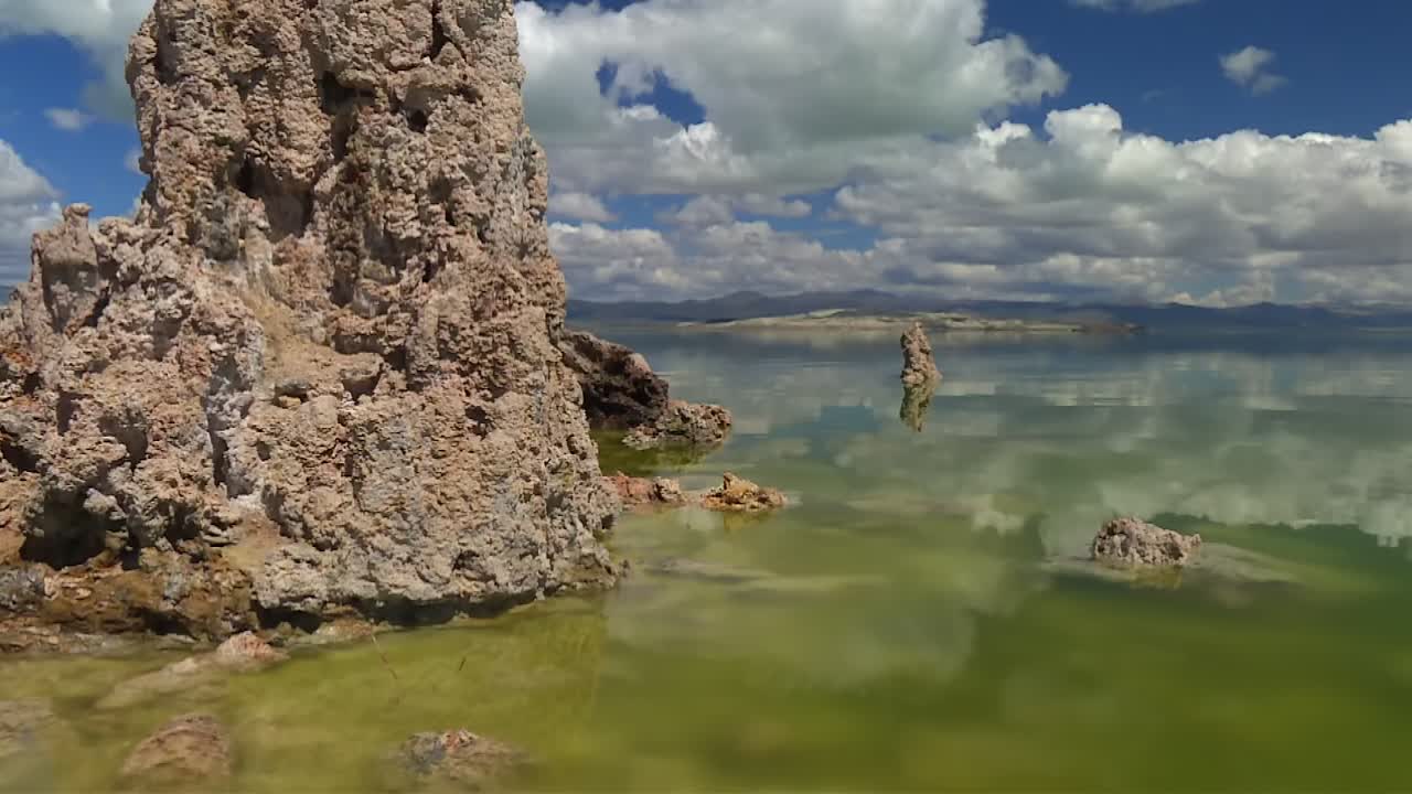 Merkittävä tuffitorni vasemmalla matalan vihreän veden äärellä, hajanaisine kivihuippuineen ja pilvineen, Mono Lake, Kalifornia.