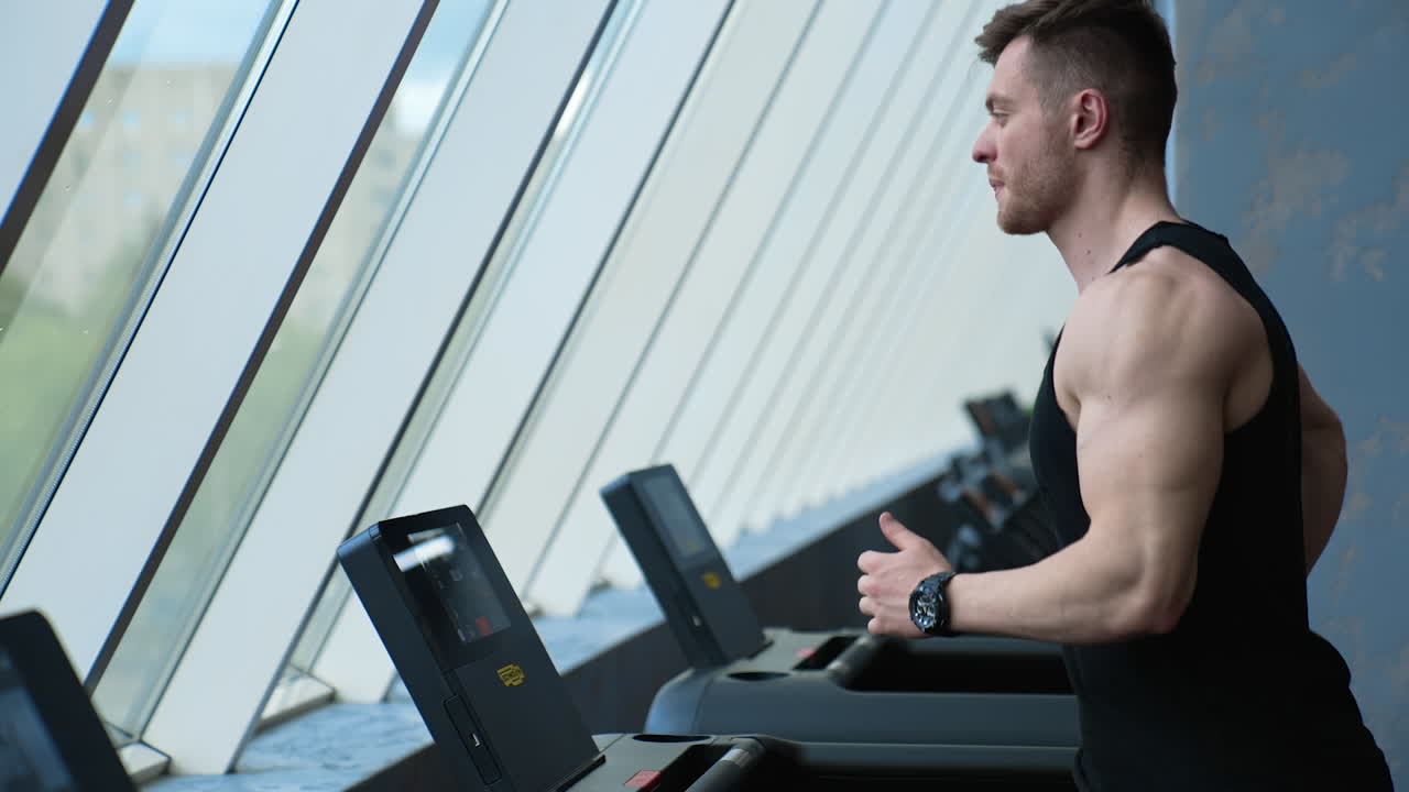 Adam spor salonunda koşu bandında koşuyor. Genç atletik adam spor salonunda koşu bandında egzersiz yapıyor ve koşuyor.