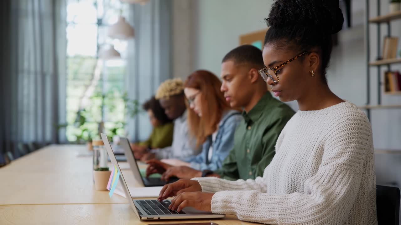 Side angle video of diverse group working on laptops in a modern, bright office space
