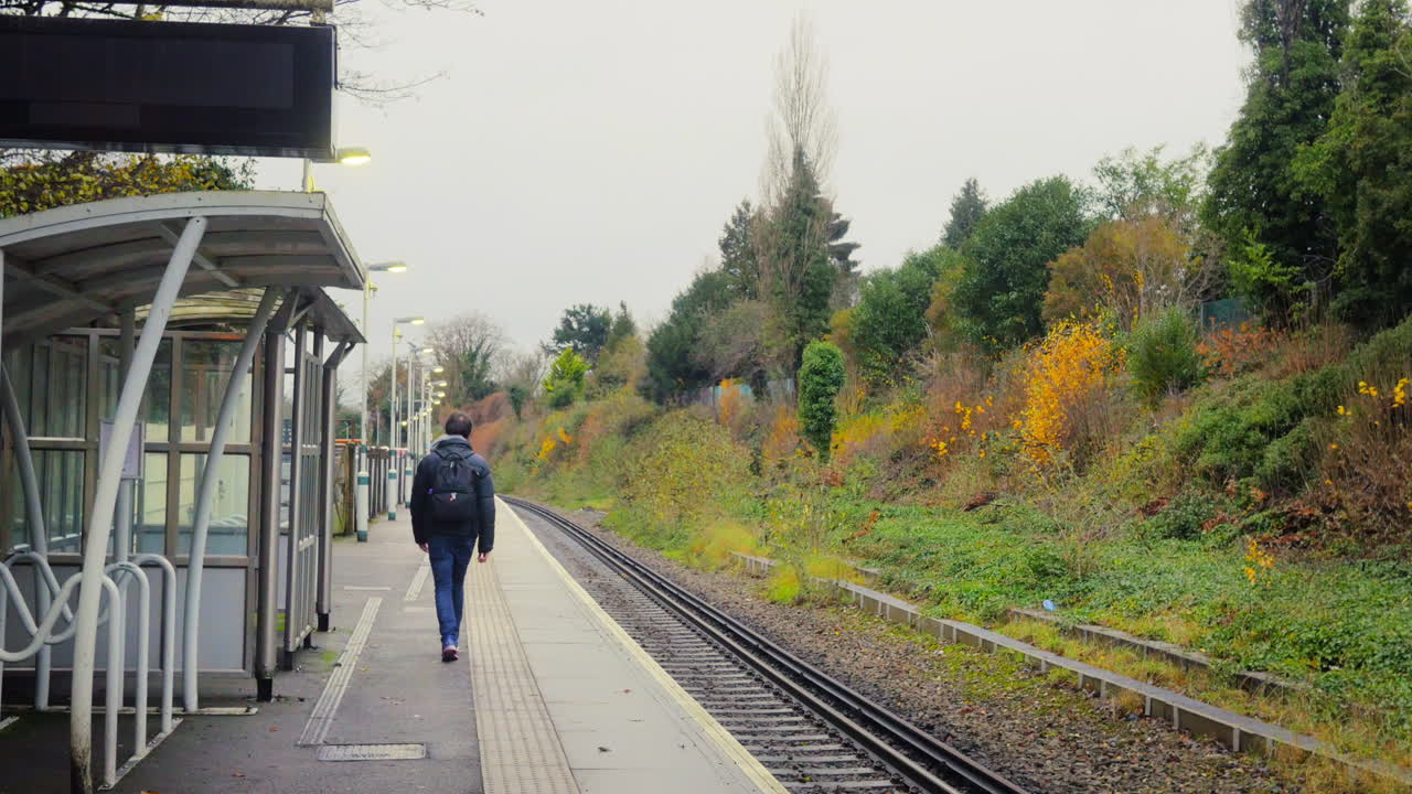 WIDE SHOT of a young male on an empty train station with day pack.