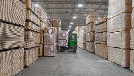 worker with reach forklift loads stack of timber planks in warehouse