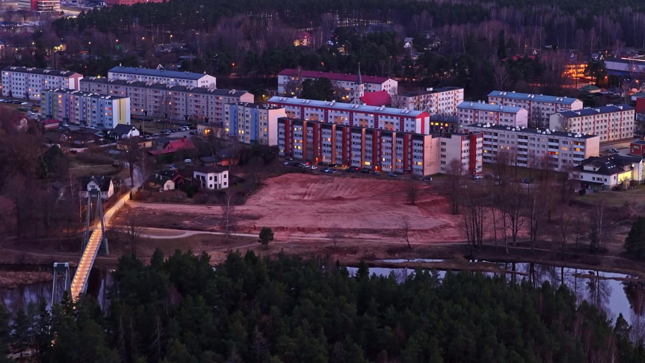Flyfoto av et boligområde i Valmiera by med en skog og en bro i skumringen i Latvia
