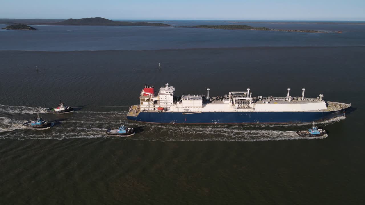 Tugboats providing safe passage to a large bulk cargo ship leaving the safety of an industrial harbor port. Drone view