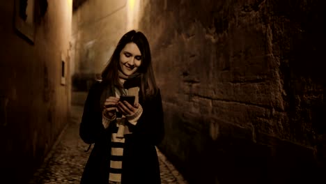 young stylish woman going late at night through the deserted lane, street and using the smartphone, chatting