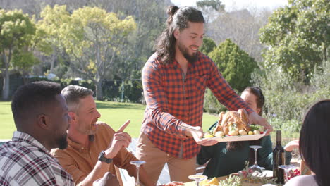 happy diverse male and female friends serving thanksgiving celebration meal in sunny garden