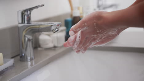 Close-up-of-biracial-woman-washing-hands-in-bathroom,-slow-motion