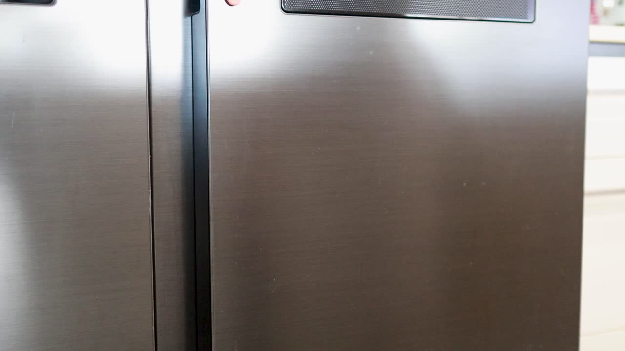 A person opens a refrigerator to pick up fresh vegetables, highlighting a clean kitchen environment with bright lighting