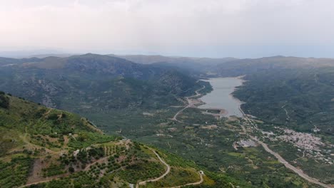 Birds-eye-view-of-beautiful-valley-surrounded-by-tall-dense-green-mountains-on-a-cloudy-day