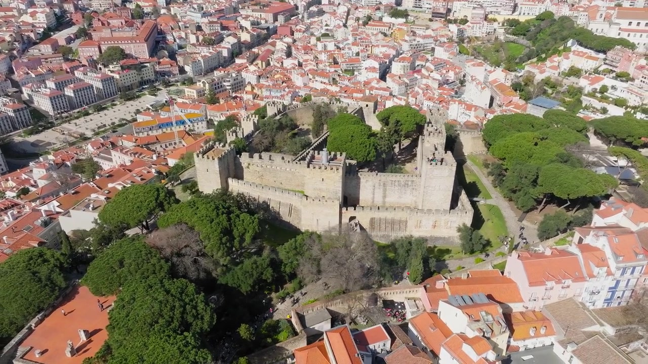 Lenta panoramica con drone del Castello di São Jorge, Lisbona a mezzogiorno. Giornata luminosa e soleggiata, cielo azzurro limpido. Castello storico che domina la città. Portogallo