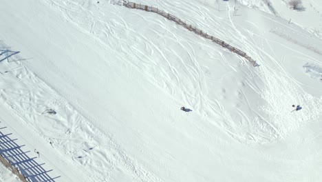 Aerial-view-looking-down-over-winter-tourist-skiing-down-snowy-Farellones-ski-resort-steep-mountain-slope,-Santiago,-Chile