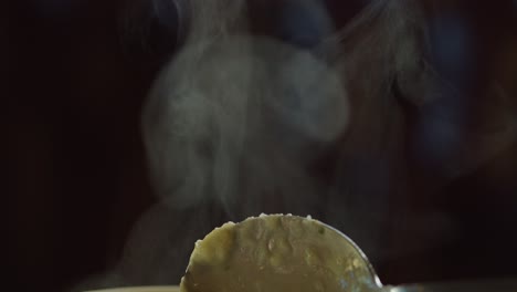 a spoon lifts hot soup, releasing swirling steam in a dark, softly lit environment. shallow focus and slow camera movement emphasize texture and warmth