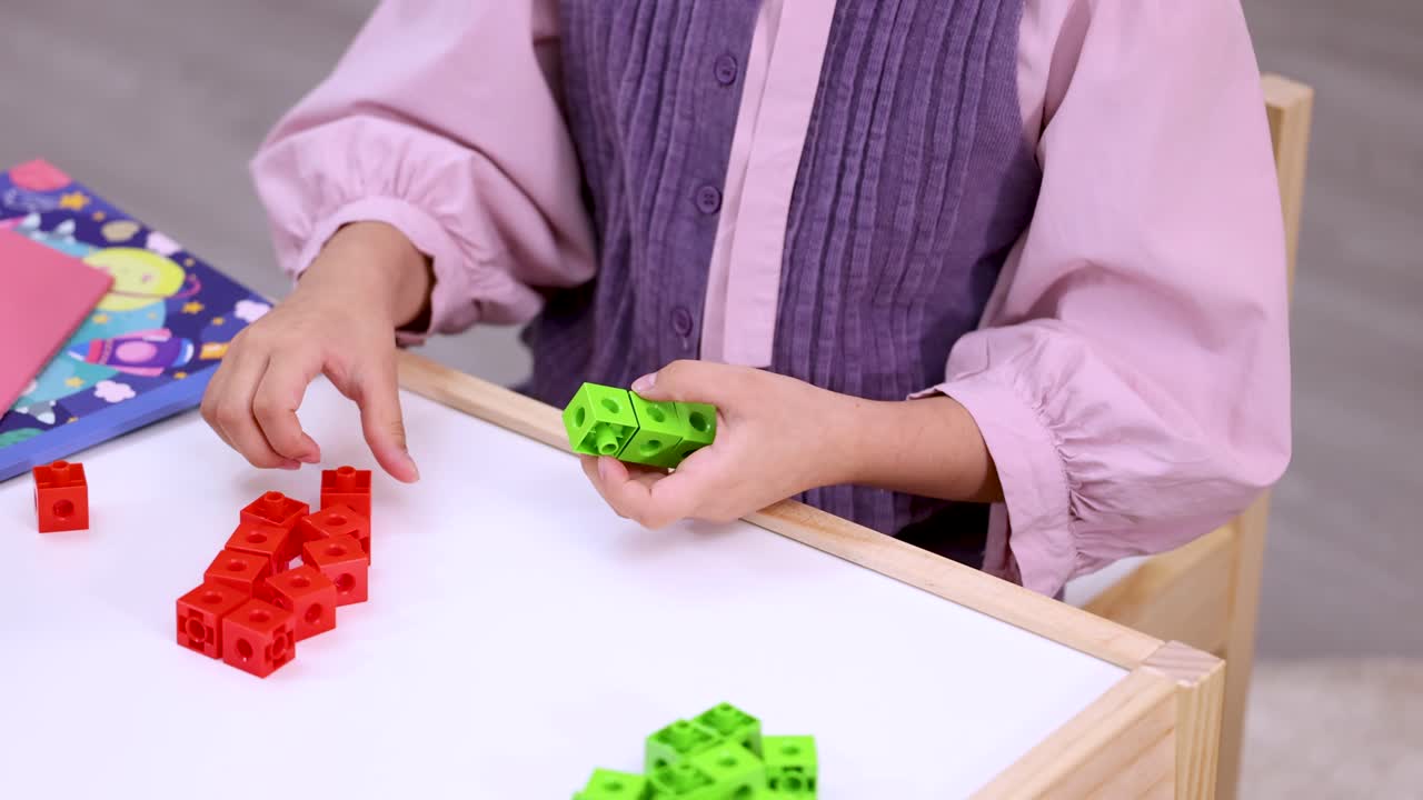 Elementary student assembles red and green counting cubes on white table in bright classroom
