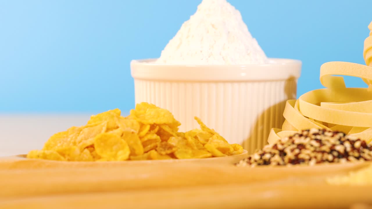 A variety of grains, pasta, and bread arranged against a vibrant blue backdrop, highlighting texture and color contrast