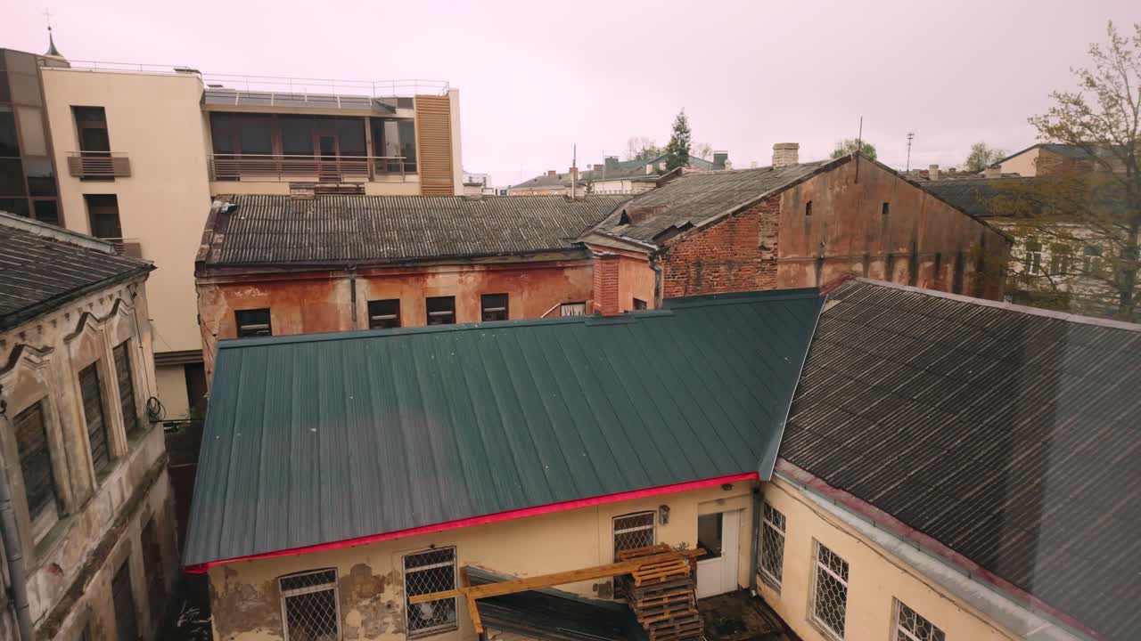 Elevated perspective over ageing Daugavpils back-lot: rusted corrugated roofs, cracked plaster walls and stacked pallets below. Daugavpils, Latvia (Daugavpils, Latvija)