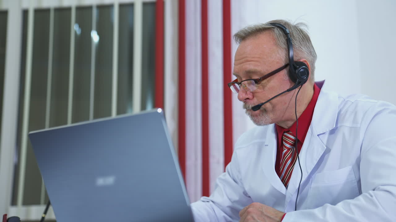Médico hablando en videollamada desde el consultorio. Médico sénior sentado en el escritorio y hablando a cámara.