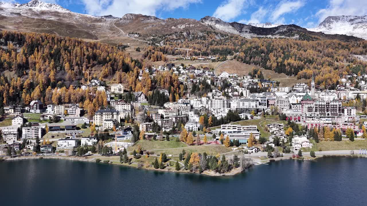 Drone flight over alpine town by a tranquil lake with autumn trees and mountains in Switzerland
