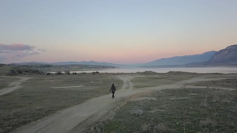 Forward-drone-shot-of-a-girl-running-to-the-lake