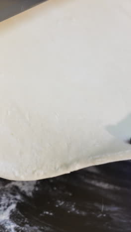 Metal roller machine for flattening dough. Gloved hands of a chef pull a flat piece of pastry from a culinary device. Close up. Vertical video