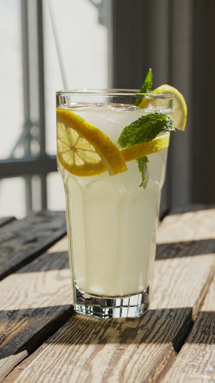 Close-up video of a refreshing lemonade with lemon slices and mint in a tall glass, shot at eye