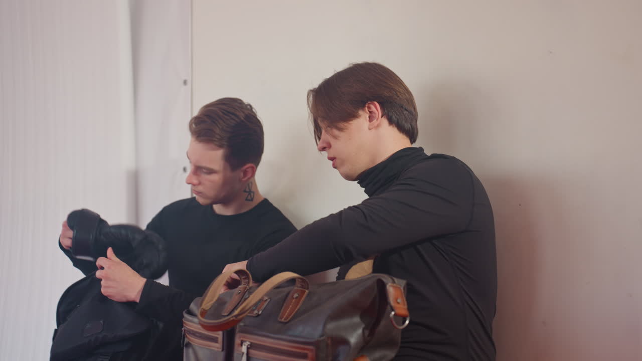 Policeman in black uniform inside martial arts gym preparing for training, sits near punching bag with focused expression, showing determination and readiness during practice environment with red mat
