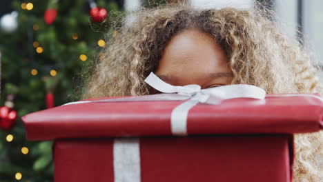 retrato de una mujer que lleva una pila de regalos de navidad de pie junto al árbol en casa