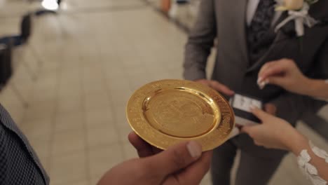 Close-up-of-wedding-rings-of-newlyweds-in-golden-plate-with-holy-water-during-the-ceremony-matrimony