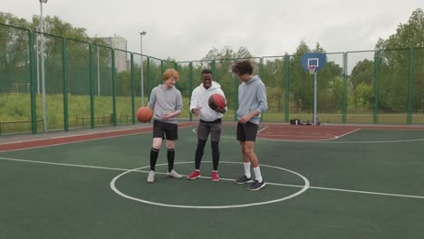 three friends with basketballs on basketball court, smiling and looking at camera