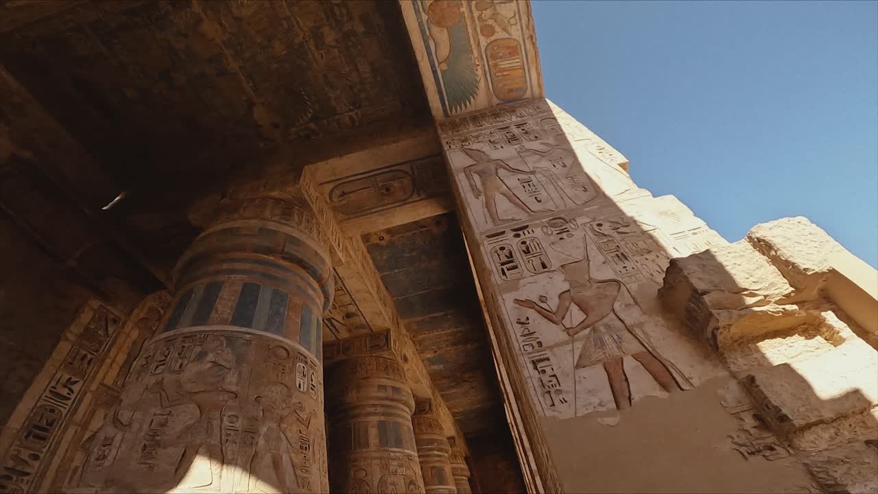 A stunning upward angle view of an ancient Egyptian temple entrance adorned with vibrant hieroglyphic carvings and partially preserved paintwork. The bright blue sky.