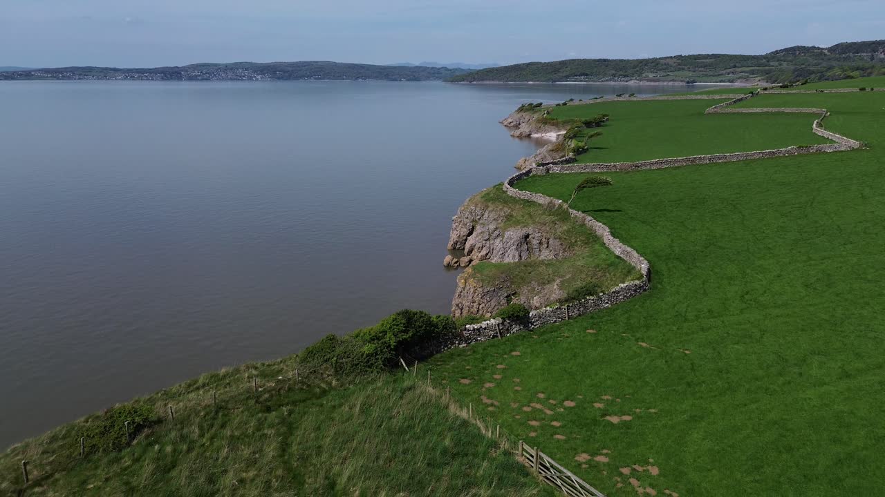Lake district coastal farming meadow aerial view descent to stone wall curving across Morecambe bay
