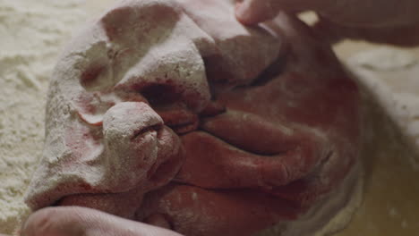 a person kneading red food coloring cookie dough into flour, static close up