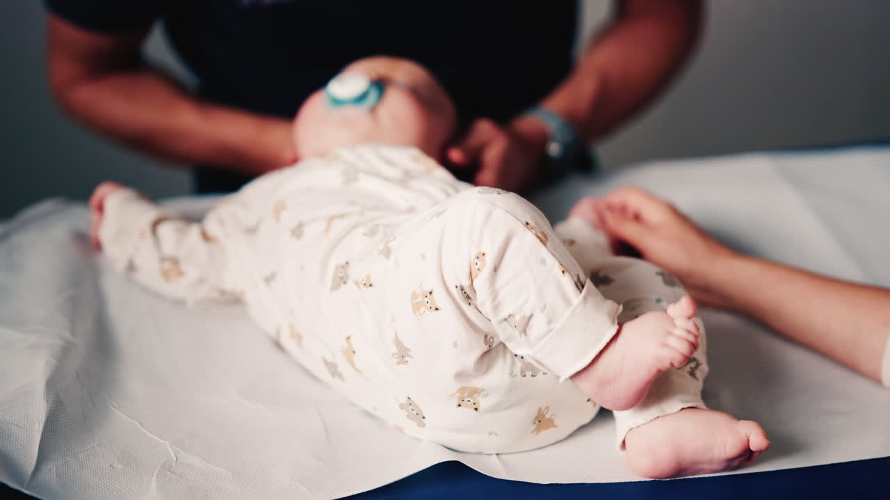 Close up of an infant's legs and feet while caregivers gently reposition the baby during a care or examination session