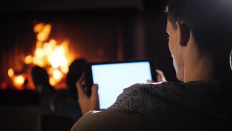 confident man with a tablet in his hands resting at home in front of the fireplace where the fire is