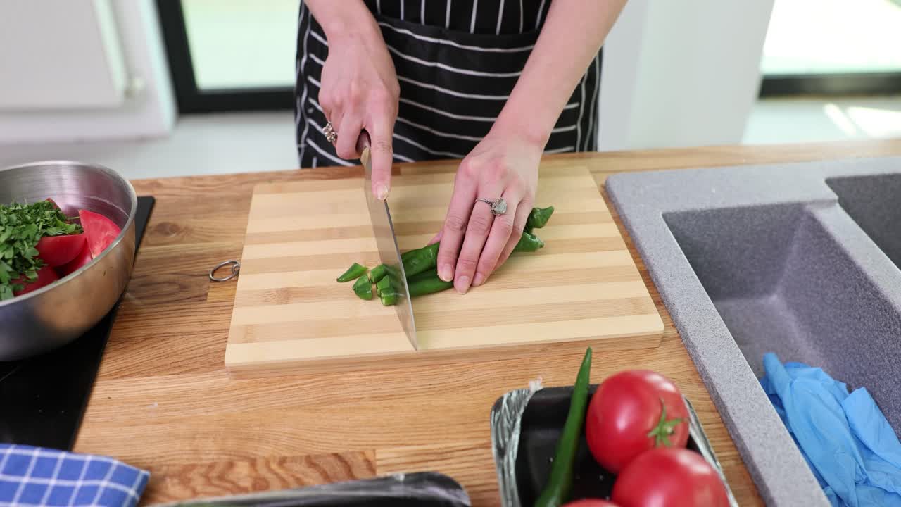 Person Chopping Green Peppers on a Wooden Cutting Board in a Kitchen
