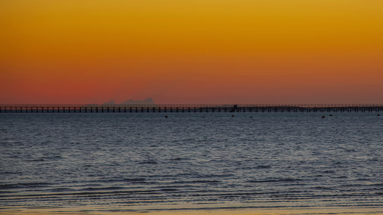 A golden sun rising behind a huge pier in the ocean