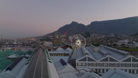 Forwards-fly-above-Victoria-Wharf-Shopping-Centre-in-evening.-Sea-waterfront-in-city-at-dusk.-Cape-Town,-South-Africa