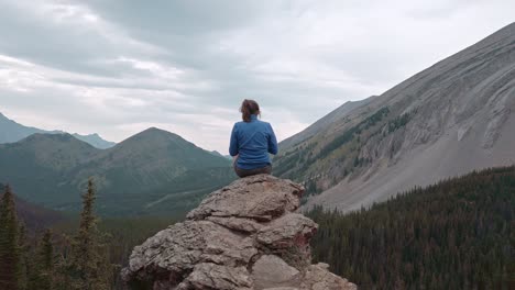 Hiker-sitting-on-ledge-taking-photos-of-mountains-approached-Kananaskis-Alberta-Canada