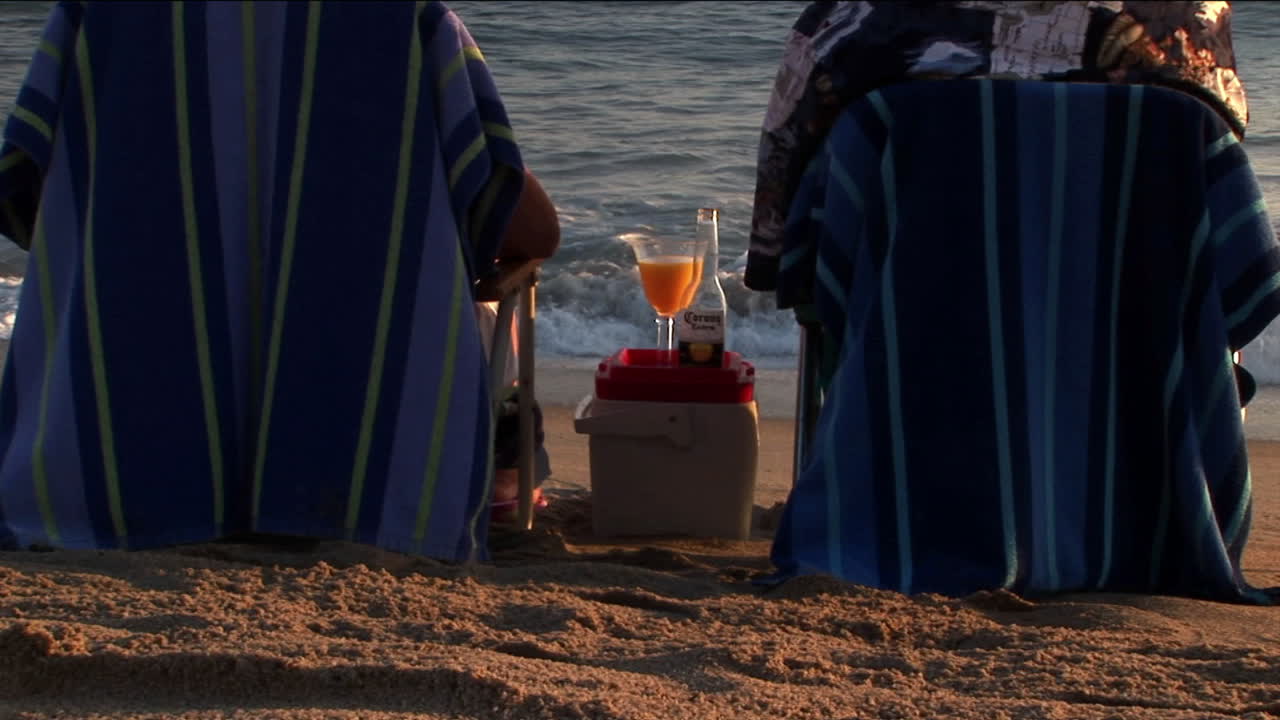 노인 부부는 해변 의자에서 파도에 건배합니다.