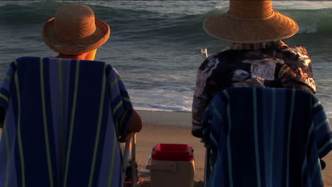 una pareja de ancianos hace un brindis por las olas del mar desde sus sillas de playa