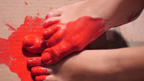 close-up on bare feet of performance artist painting on cardboard with her feet and red paint | slow motion of acrylic paint muddy feet