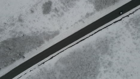 Car-driving-on-icy-road-in-landscape-covered-in-snow,-overhead-drone