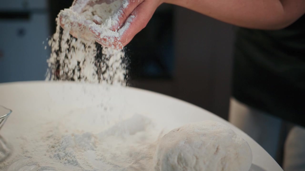 Hands knead dough on floured surface. Flour dusts as hands work. Person focused, calm, and skilled. Ideal for cooking, baking, or food tutorials. Perfect for recipe videos or culinary content