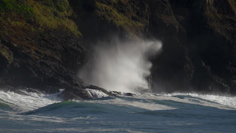 turbulent ocean waves cresting and crashing on a mossy black cliffside of a mountain - fixed slow-mo shot