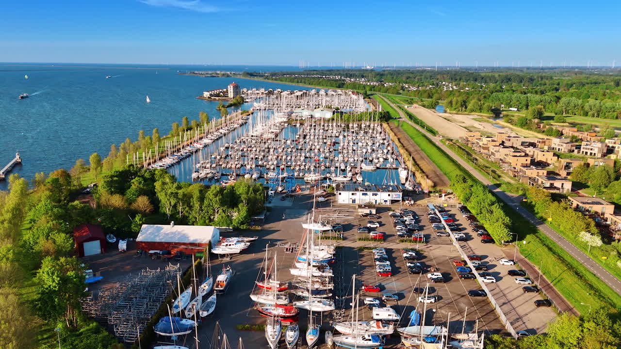 Approaching the boats on the shore near the parking lot. Numerous yachts stand on the anchor in yacht club. Green cityscape of Lelystad, the Netherlands at backdrop.