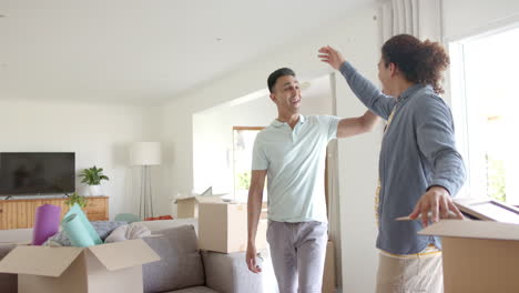 happy diverse gay male couple embracing in new home with packing boxes, copy space, slow motion