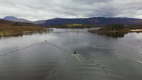 ángulo de cámara lenta aérea cinematográfica del sobrevuelo de drones siguiendo a tres barcos que se acercan a los estrechos en loch lomond en escocia