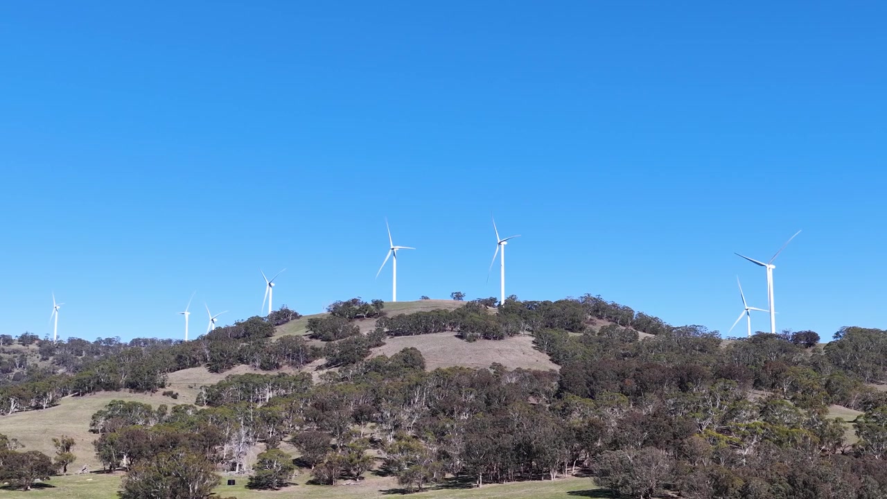 Turbine eoliche che ruotano su un pendio erboso sotto un cielo azzurro e limpido