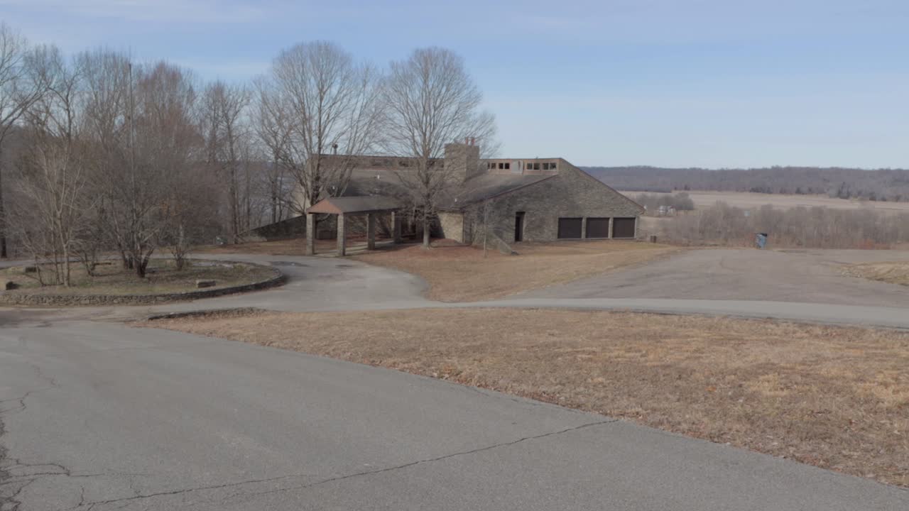 Abandoned Lodge Sitting on a Hill Overlooking the Countryside during Winter.  Static Shot showing the Road, Front of the Lodge, and the Surrounding Forest and Grassy Areas.
